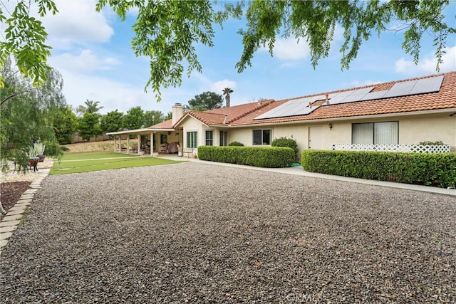 ranch-style home featuring roof mounted solar panels, stucco siding, a tile roof, and a chimney