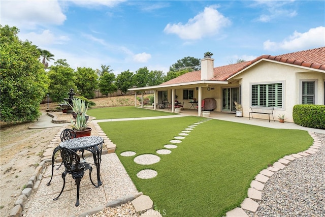 back of property with a chimney, a tile roof, a lawn, a patio area, and stucco siding