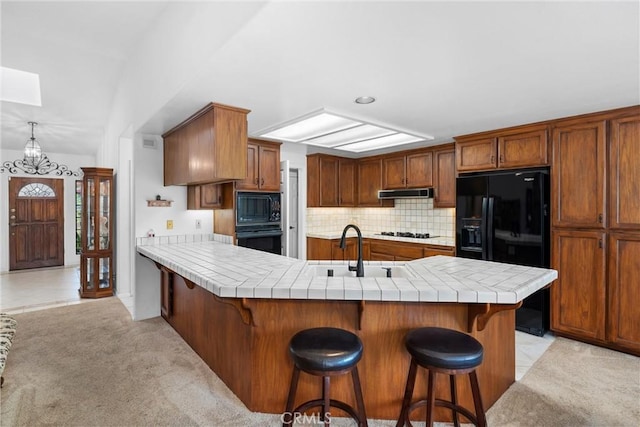 kitchen featuring a sink, a breakfast bar area, tile counters, backsplash, and black appliances