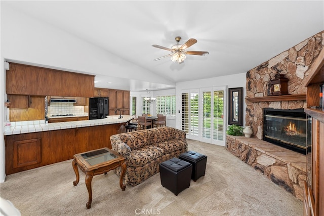 living area with a stone fireplace, a ceiling fan, lofted ceiling, and light carpet