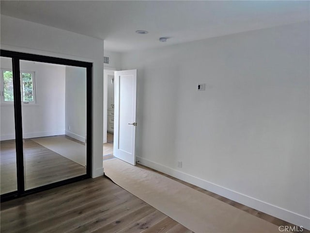 unfurnished bedroom featuring baseboards, a closet, wood finished floors, and visible vents