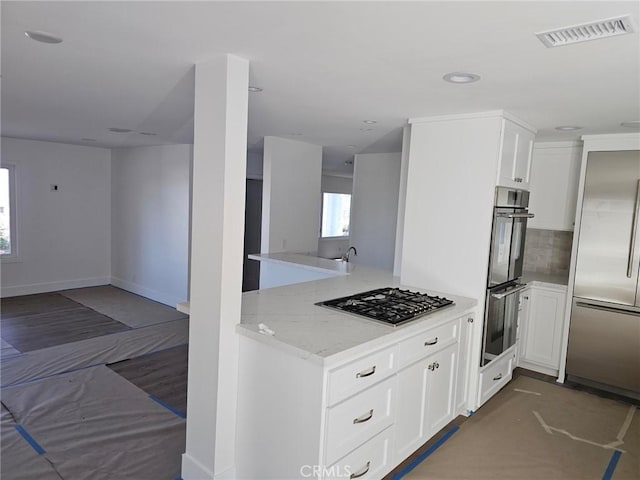 kitchen with visible vents, appliances with stainless steel finishes, light stone countertops, a peninsula, and open floor plan