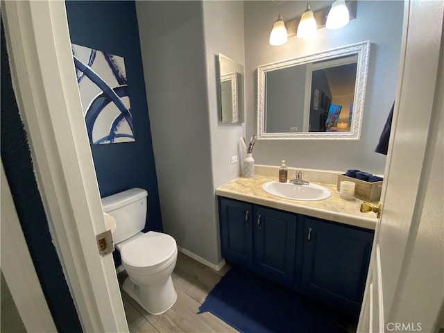 half bath with vanity, baseboards, wood finished floors, and toilet