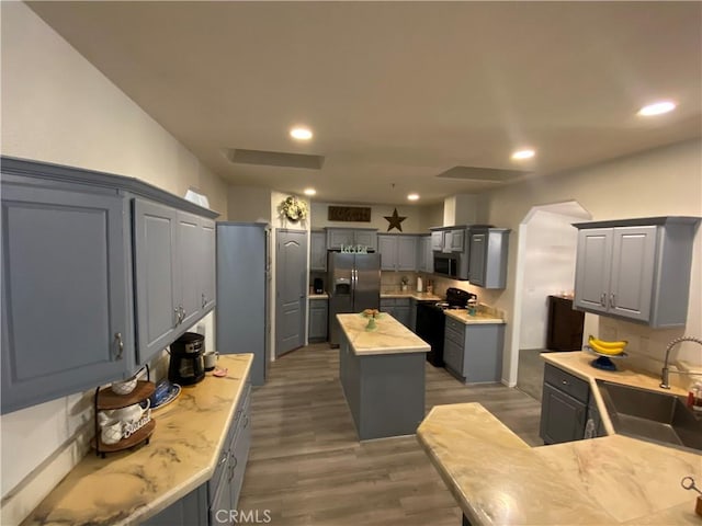 kitchen with a sink, wood finished floors, gray cabinetry, a kitchen island, and appliances with stainless steel finishes