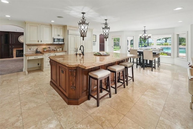 kitchen with stainless steel microwave, cream cabinetry, light stone counters, a chandelier, and recessed lighting