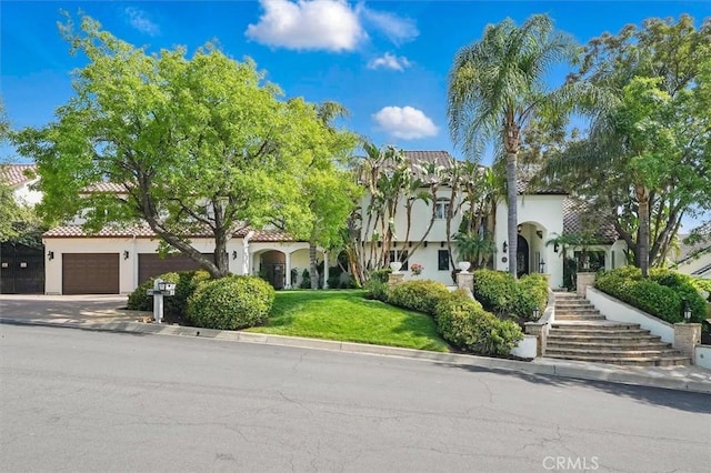 mediterranean / spanish home with stucco siding, stairway, a front yard, and driveway