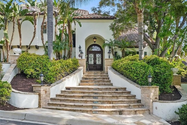 property entrance featuring french doors, a tile roof, and stucco siding