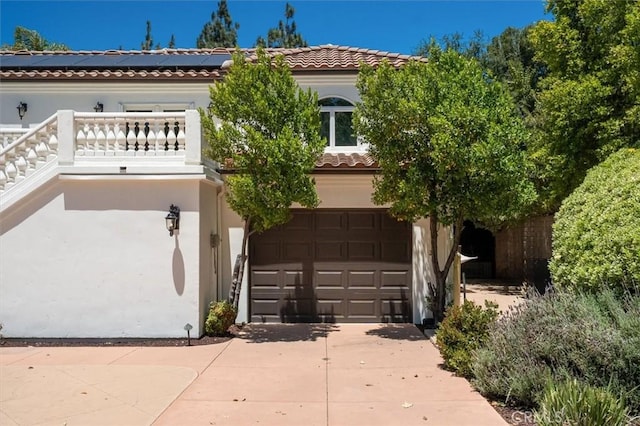 view of front facade featuring concrete driveway, roof mounted solar panels, stucco siding, a garage, and a tiled roof