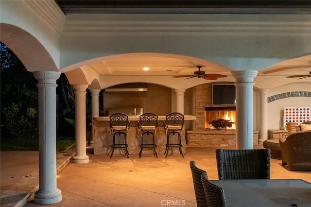 view of patio / terrace featuring an outdoor bar, ceiling fan, and a lit fireplace