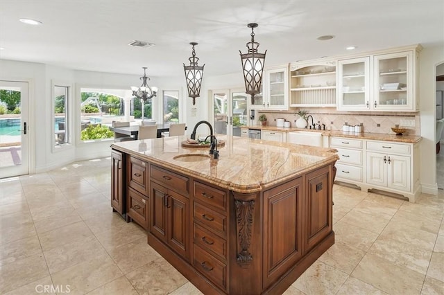 kitchen featuring a sink, backsplash, a kitchen island with sink, light stone countertops, and recessed lighting