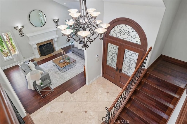 foyer entrance with stairway, baseboards, a chandelier, and a fireplace