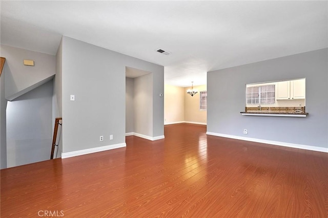 spare room with an inviting chandelier, baseboards, and wood finished floors