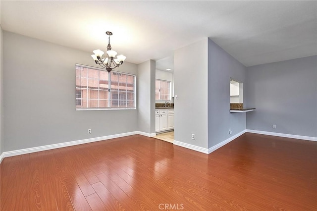 empty room with a sink, baseboards, a notable chandelier, and wood finished floors