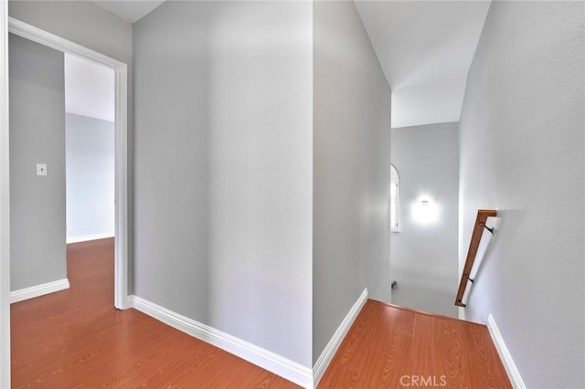 hall featuring baseboards, wood finished floors, and an upstairs landing