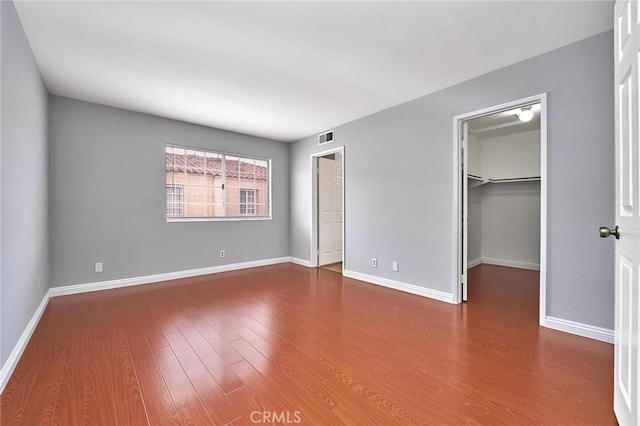 unfurnished bedroom featuring a walk in closet, visible vents, wood finished floors, baseboards, and a closet
