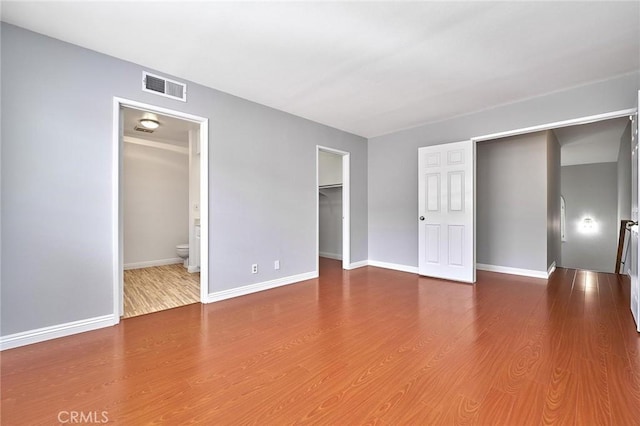unfurnished bedroom featuring a spacious closet, baseboards, wood finished floors, and visible vents