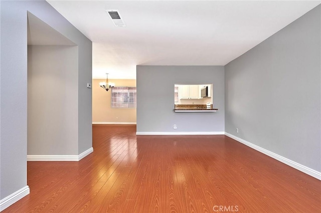 unfurnished living room with baseboards, an inviting chandelier, wood finished floors, and visible vents