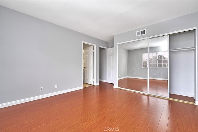 unfurnished bedroom featuring baseboards, visible vents, wood finished floors, and a closet