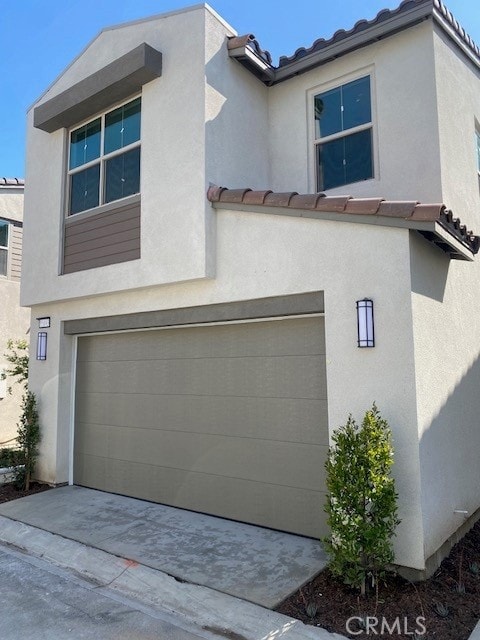 view of side of home featuring an attached garage, driveway, a tile roof, and stucco siding