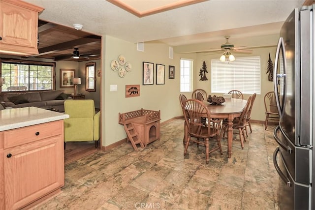 dining room with ceiling fan, beamed ceiling, baseboards, and stone finish floor