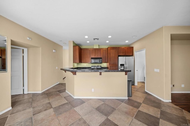kitchen with a kitchen bar, black microwave, a sink, stainless steel fridge with ice dispenser, and baseboards