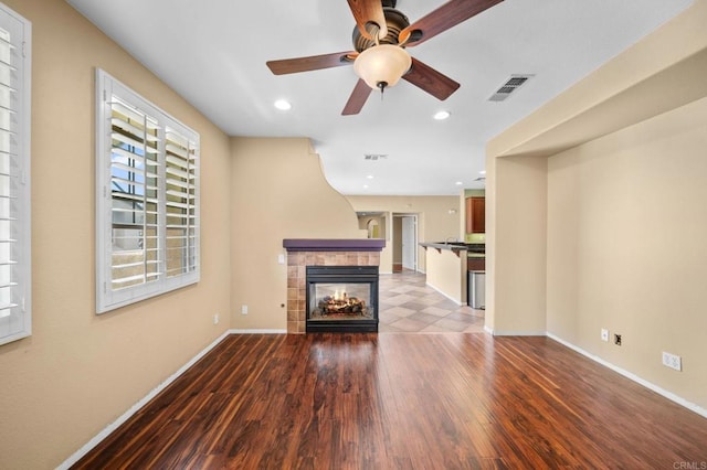 unfurnished living room with visible vents, wood finished floors, baseboards, a tiled fireplace, and a ceiling fan