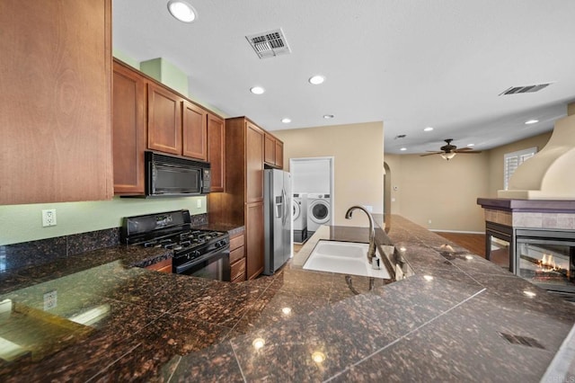 kitchen featuring visible vents, washer and dryer, brown cabinets, a sink, and black appliances