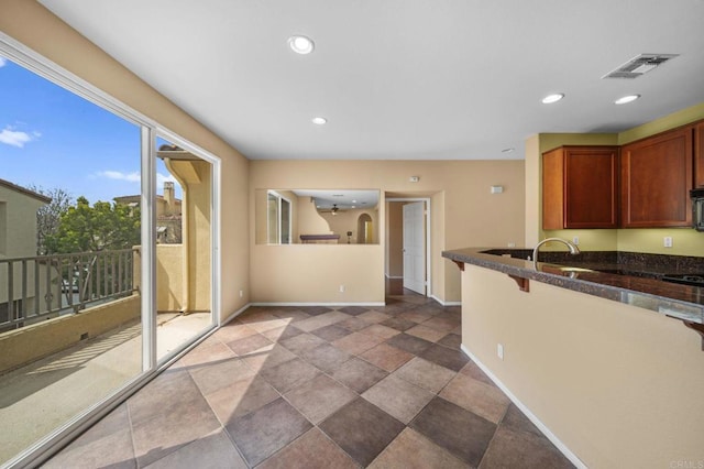 kitchen featuring stone finish floor, visible vents, baseboards, dark stone countertops, and recessed lighting