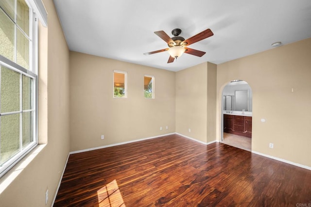 empty room with arched walkways, baseboards, a ceiling fan, and wood finished floors