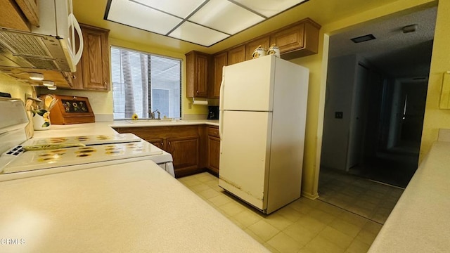 kitchen featuring a sink, light countertops, freestanding refrigerator, and brown cabinetry