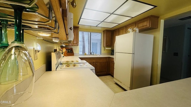 kitchen featuring brown cabinetry, freestanding refrigerator, stove, light countertops, and a sink