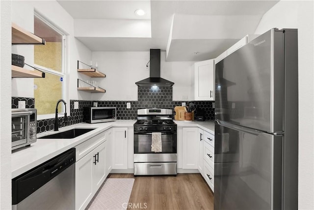 kitchen with wall chimney range hood, white cabinets, open shelves, a sink, and stainless steel appliances