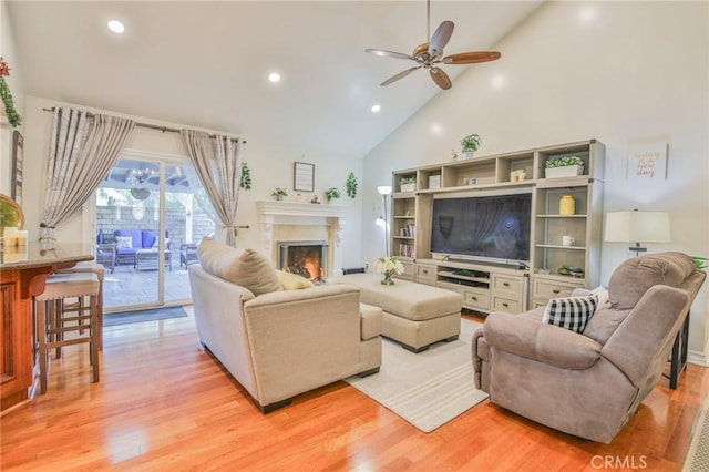 living room featuring light wood finished floors, high vaulted ceiling, a glass covered fireplace, a ceiling fan, and recessed lighting