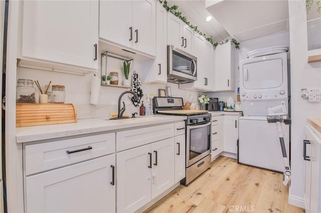 kitchen with appliances with stainless steel finishes, a sink, light wood-style flooring, white cabinetry, and stacked washer / dryer