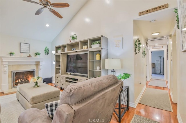 living area with a premium fireplace, high vaulted ceiling, a ceiling fan, baseboards, and wood finished floors