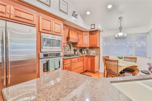 kitchen with an inviting chandelier, built in appliances, premium range hood, backsplash, and vaulted ceiling