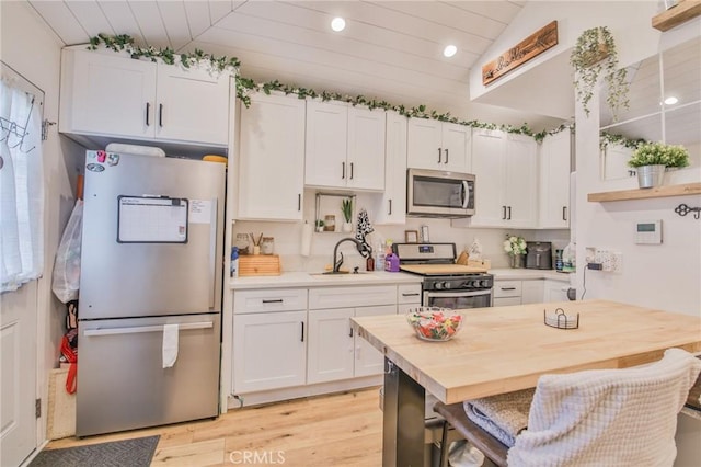 kitchen with white cabinets, open shelves, appliances with stainless steel finishes, a sink, and light wood finished floors