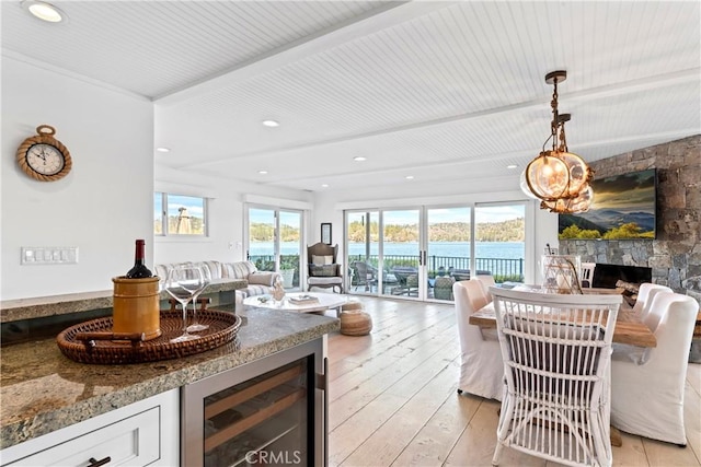 living room with beverage cooler, a stone fireplace, recessed lighting, light wood-type flooring, and a water view