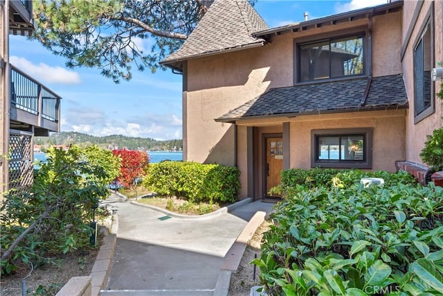 view of exterior entry with a shingled roof, stucco siding, and a water view
