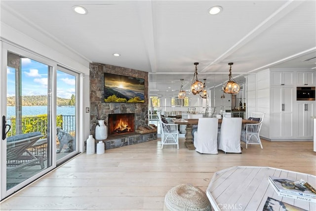 living room with an inviting chandelier, beamed ceiling, light wood-style floors, a stone fireplace, and recessed lighting