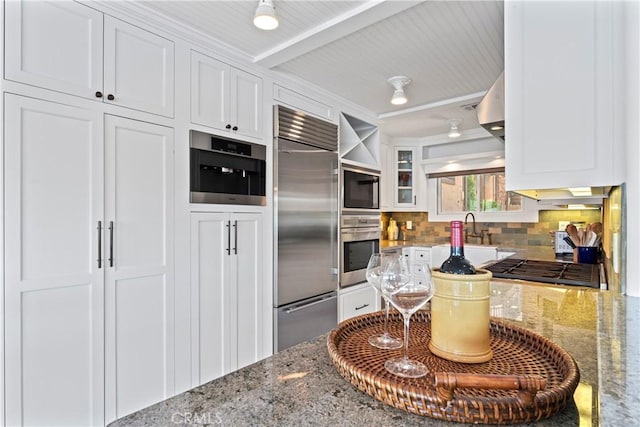 kitchen featuring built in appliances, white cabinets, and tasteful backsplash