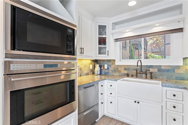kitchen featuring tasteful backsplash, a sink, light stone counters, stainless steel appliances, and white cabinetry