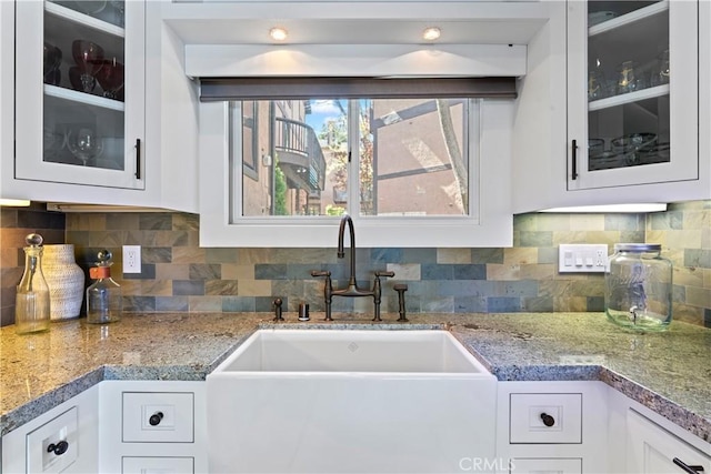 kitchen featuring a sink, glass insert cabinets, tasteful backsplash, and white cabinetry