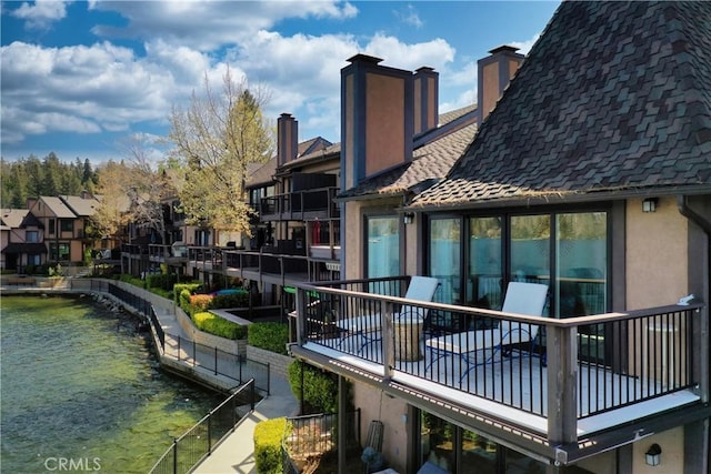 rear view of house featuring a balcony, stucco siding, a chimney, a water view, and a residential view