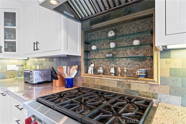kitchen featuring backsplash, light stone countertops, glass insert cabinets, custom range hood, and white cabinetry