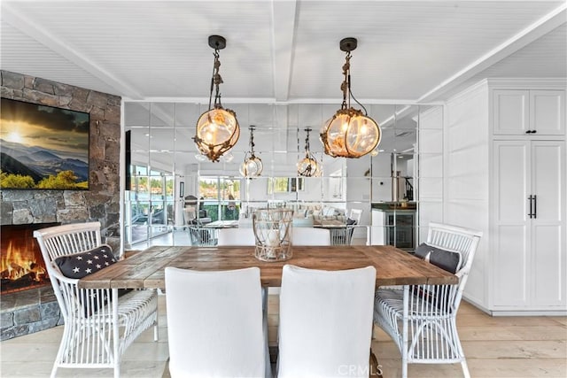 dining room featuring a fireplace, light wood-style flooring, and beam ceiling