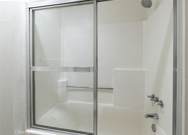 full bath featuring a textured wall and combined bath / shower with glass door