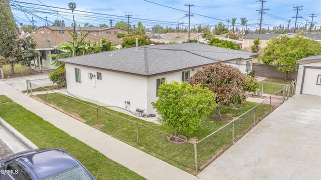 view of side of home featuring roof with shingles, a lawn, a residential view, fence, and stucco siding