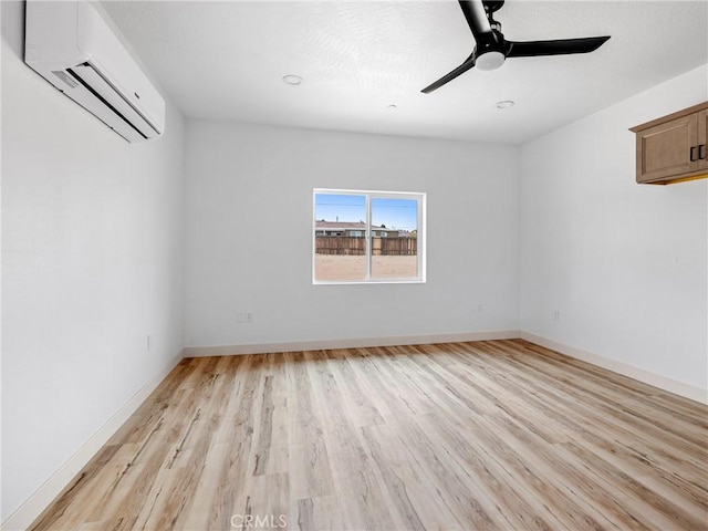 empty room featuring ceiling fan, a wall mounted AC, baseboards, and light wood finished floors