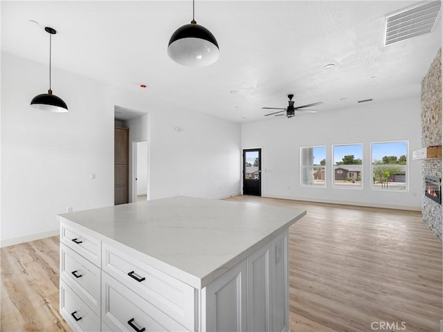 kitchen featuring visible vents, a stone fireplace, white cabinets, a ceiling fan, and light wood finished floors